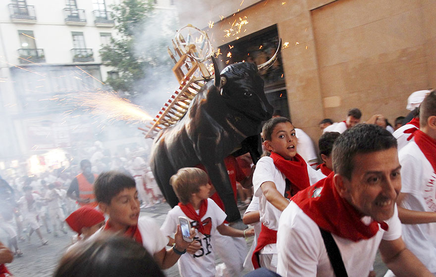 La gente huye del “Toro en llamas”, un hombre que lleva a cuestas una estructura metálica cubierta por fuegos artificiales en el segundo día de la fiesta de San Fermín en Pamplona, Espa?a, el 7 de julio de 2015. Los visitantes que llegan al festival de nueve días participan en actividades como la carrera con toros, una maratón por la ma?ana temprano de media milla en la que seis toros deben llegar a la plaza donde los torearán por la tarde. Además hay procesiones de gigantes, conciertos, “toros en llamas”, fuegos artificiales y mucha comida, bebida y baile. [Agencias de fotografía]