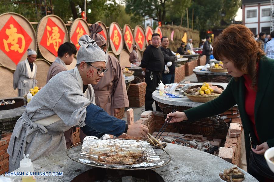 Una turista prueba pescado a la parrilla durante la 8 Feria del Pescado, en el municipio de Hefu, provincia de Zhejiang, en el este de China, el 2 de diciembre de 2016. (Xinhua/Huang Zongzhi)