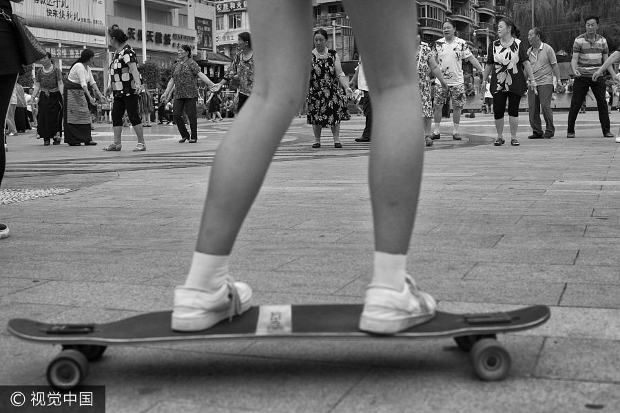 Una ni?a en patineta pasa junto a un grupo de hombres y mujeres que bailan en Luding, provincia de Sichuan, el 19 de agosto de 2016. [Foto / VCG]