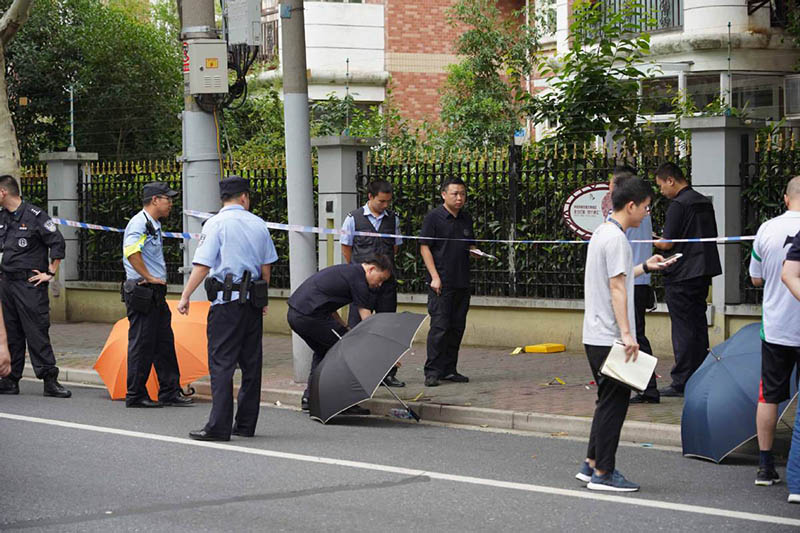 La policía cubre con paraguas la sangre en la escena del ataque con cuchillo ocurrido en Shanghai. [Foto: Gao Erqiang]. 