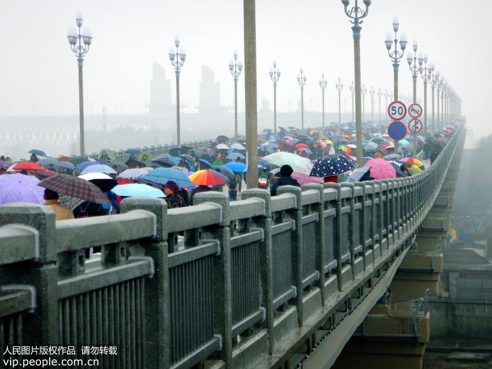 La gente en Nanjing desafía a la lluvia cruzando el recién renovado puente sobre el río Yangtse