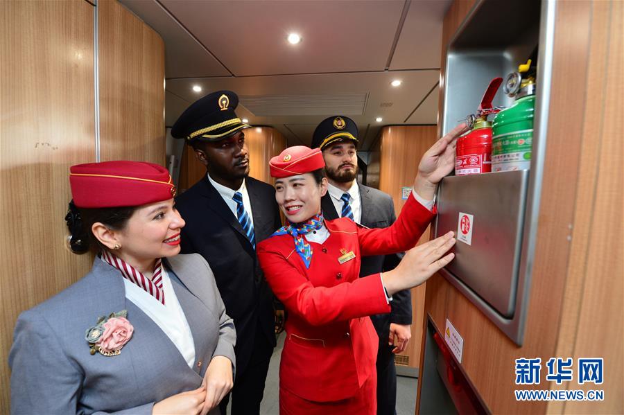 El 20 de enero, en un tren de alta velocidad de la estación ferroviaria Xi'an Norte, una azafata (tercera desde la izquierda) explica el uso de equipo contra incendios a los estudiantes voluntarios extranjeros.