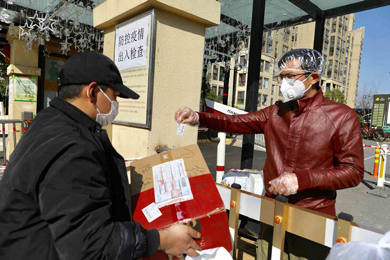 Un hombre busca su compra en la puerta de una comunidad residencial en Wuhan, provincia de Hubei, 18 de febrero del 2020.?[Foto: Zhu Xingxin / China Daily]