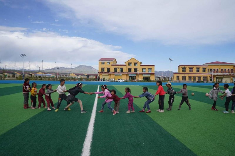 Ni?os juegan en un campo de fútbol en la Aldea Cultural Amdo, un proyecto de reasentamiento para familias pobres en el condado Xinghai, provincia de Qinghai. [Foto de Feng Yongbin / China Daily]