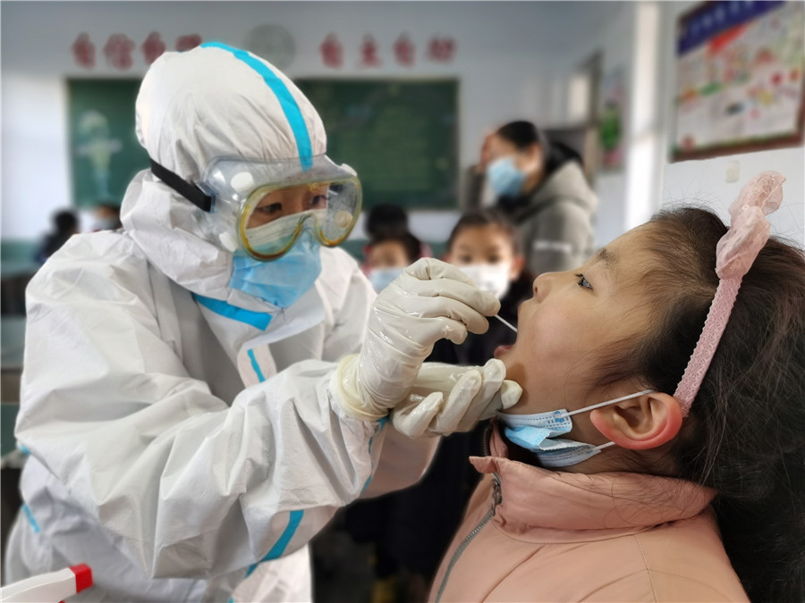 Un trabajador médico toma una muestra de garganta de una estudiante en una escuela primaria en Xingtai, provincia de Hebei, el 6 de enero de 2021. La ciudad lanzó una campa?a masiva de pruebas de ácido nucleico gratuitas después de un reciente brote de COVID-19. [Foto de Huang Tao / para China Daily]