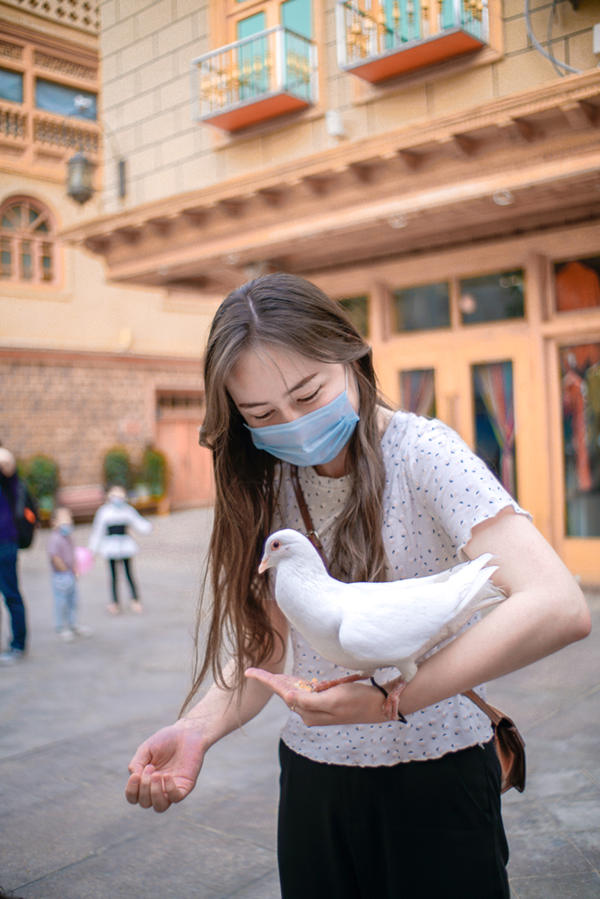 Una turista alimenta a una paloma posada en su mano a lo largo de una pasarela en Tuancheng, la calle peatonal más famosa de la ciudad de Hotan, en la región autónoma Uygur de Xinjiang, en el noroeste de China, el 22 de mayo de 2021 (Pueblo en Línea / Ma Tianyi).