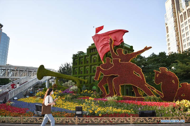 Una mujer camina junto a decoraciones florales que embellece la capitalina avenida Chang'an, 19 de junio del 2021. [Foto: Xinhua]