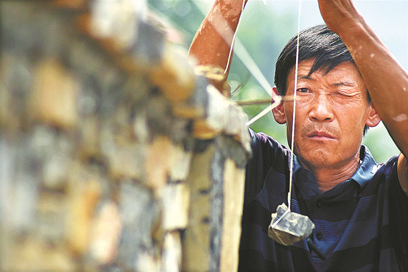 Feng Chengwen mide la verticalidad de un muro que construyó en la aldea Jibaoyu del condado Yiyuan, en la provincia de Shandong, el 10 de agosto [Foto de Zhao Dongshan y Fu Youmin / para China Daily]