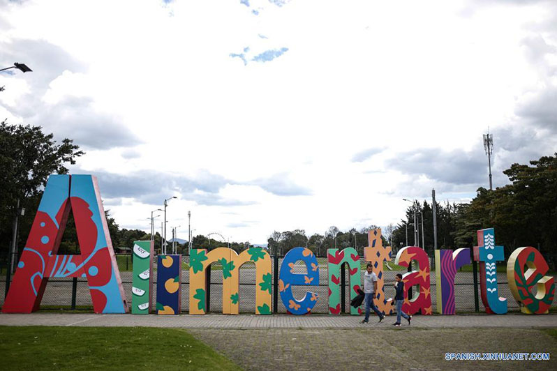 Personas caminan frente a un cartel del festival de gastronomía "Alimentarte" en el Parque Simón Bolívar, en Bogotá, Colombia, el 19 de marzo de 2022. El festival de gastronomía más importante en Colombia "Alimentarte" se llevará a cabo por cuatro fines de semana en distintos parques icónicos de la ciudad. (Xinhua/Jhon Paz)