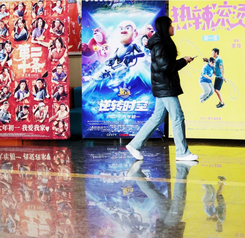 Una mujer pasa frente a carteles promocionales de películas en un cine en la ciudad de Linyi de la provincia de Shandong, en el este de China, el 15 de febrero de 2024. (Xinhua/Zhang Chunlei)