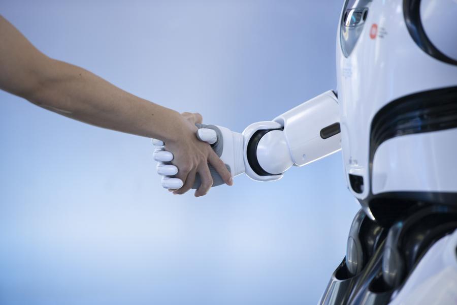 Imagen del 26 de junio de 2024 de un empleado estrechando la mano de un robot en una empresa de ciencia y tecnología, en Shenzhen, en la provincia de Guangdong, en el sur de China. (Xinhua/Mao Siqian) 