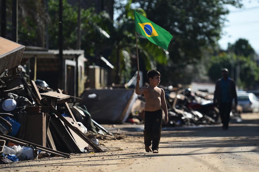 Un ni?o sostiene una bandera nacional brasile?a mientras camina por una calle afectada por las inundaciones provocadas por las fuertes lluvias, en la Isla Pintada, en la ciudad de Porto Alegre, capital del estado de Rio Grande do Sul, Brasil, el 18 de junio de 2024. (Xinhua/Lucio Tavora)